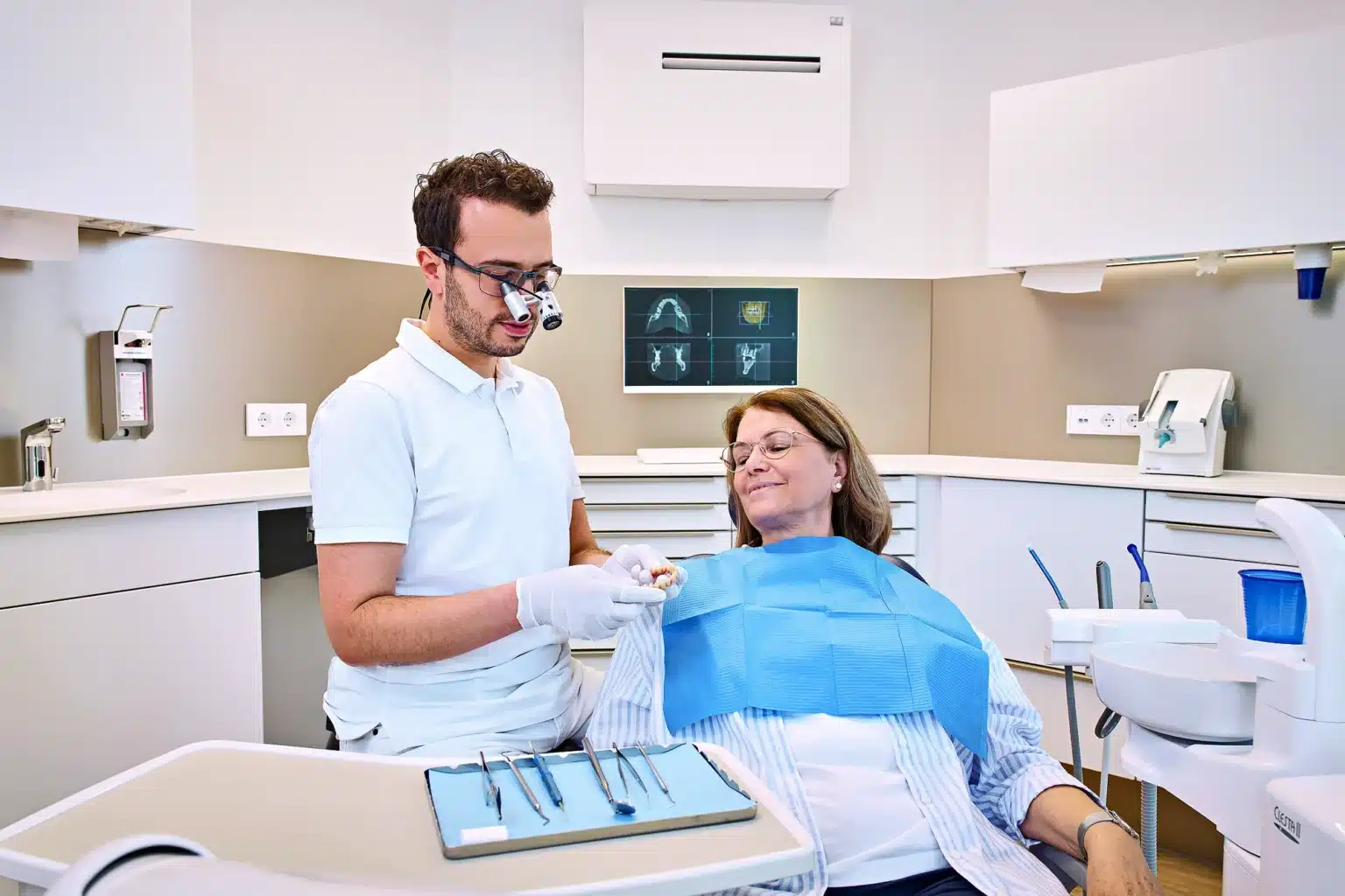 Ein modern eingerichteter Behandlungsraum, in dem eine ältere Patientin mit der Zahnärztin spricht, die ihr geduldig und mit einem Lächeln antwortet.