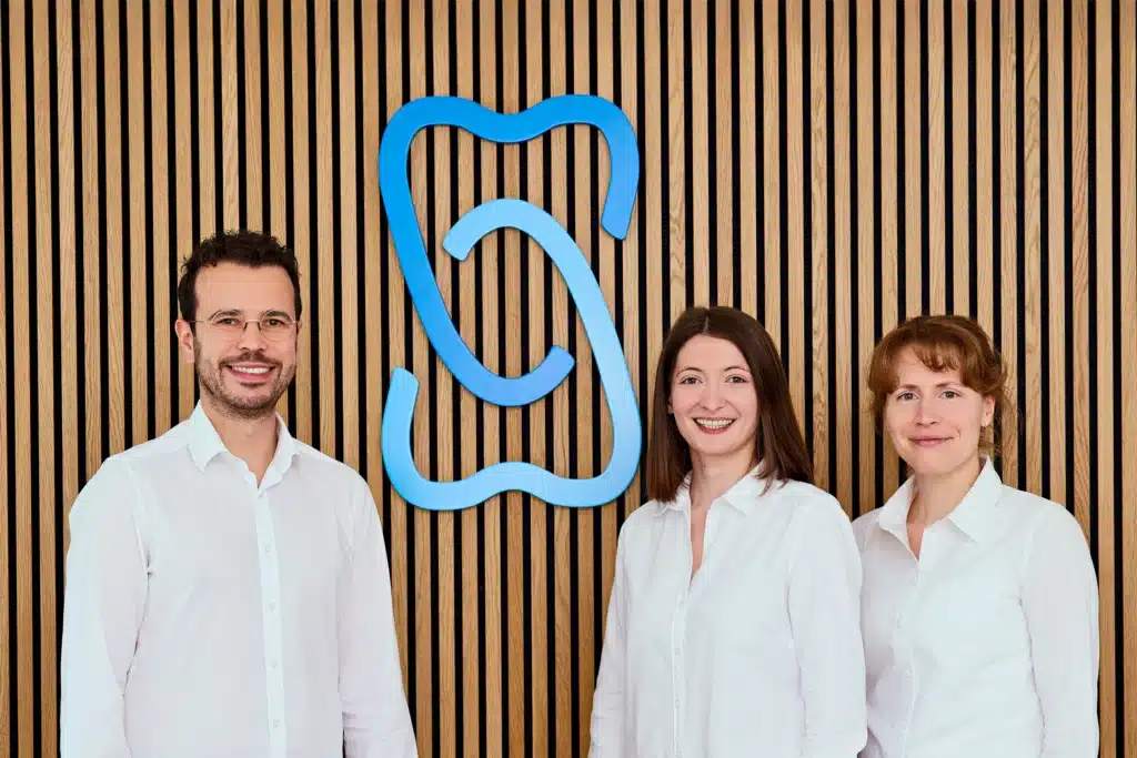 Die drei Zahnärzt*innen der Zahnarztpraxis Zahnarzt Crivitz vor dem Logo der Praxis.